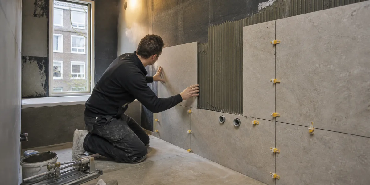 Tegelzetter plaatst grote steenlook tegels tijdens een badkamerrenovatie